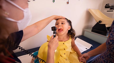 A doctor examines a child's throat with an otoscope during a check-up.