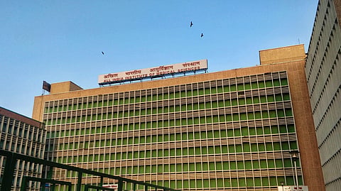 The AIIMS building stands under a clear blue sky.