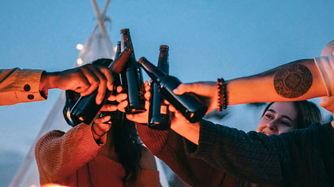 Friends clink beer bottles in a toast at dusk.