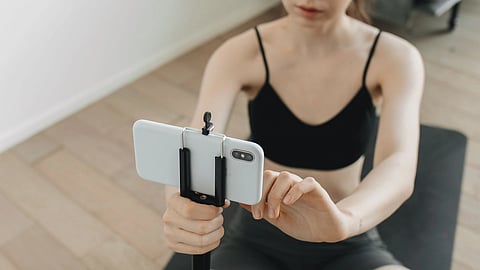 A person on a yoga mat adjusts a smartphone on a small tripod.