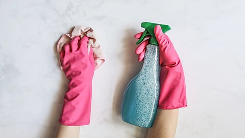 Hands in pink gloves hold a cleaning cloth and spray bottle.