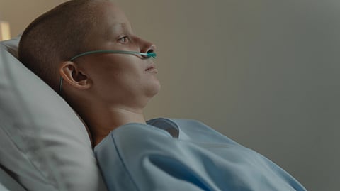 A patient lies in a hospital bed with an oxygen tube.