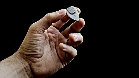 A hand holds a black guitar pick against a dark background.
