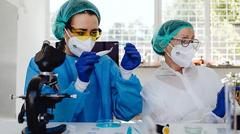 Two scientists in protective gear work in a lab.