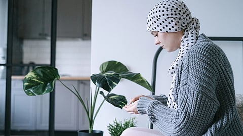 A person in a headscarf and sweater sits indoors, looking thoughtful.