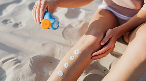 A person applies sunscreen to their leg while sitting on the beach.