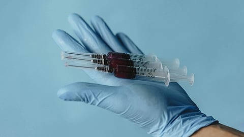 A hand with surgical glove and holding 3 injections.