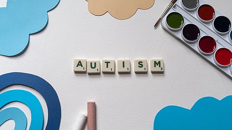 A top view shows the word “AUTISM” made with Scrabble tiles on a white background.