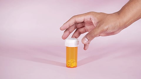 A hand reaches for a pill bottle.