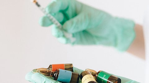 A gloved person holding a syringe and several vaccine ampoules.