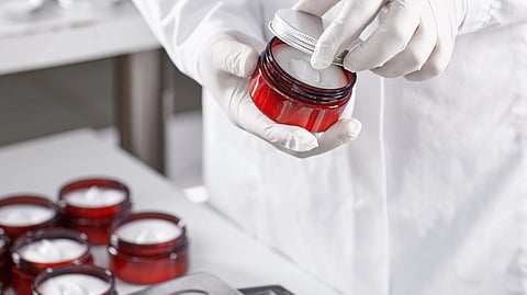 A lab worker seals a jar of cosmetic cream while other jars sit nearby.