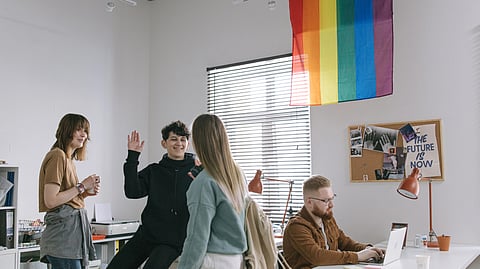 A diverse group of people holding a rainbow flag in an office.