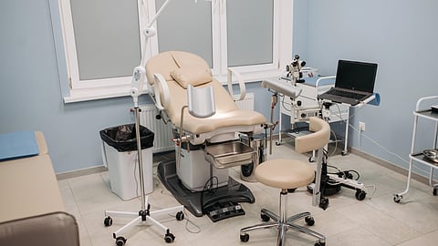 A clinic room with a chair, desk, computer, and medical equipment.