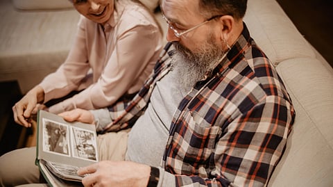 An elderly couple smiles while looking through a photo album together.