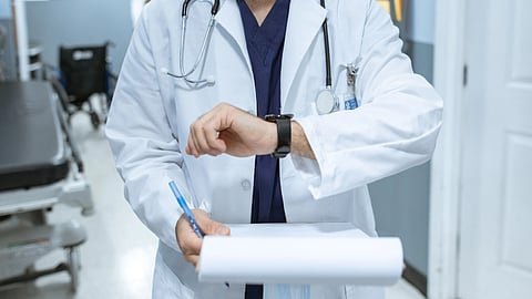A doctor in a white coat holds a clipboard.