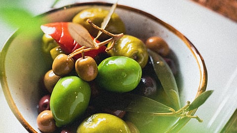 A bowl of olives beside a cup of coffee on a wooden table.