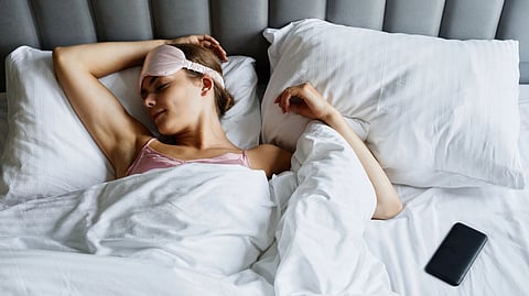 A woman lies in bed while looking at her phone.