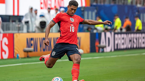 A soccer player in an England jersey kicking a ball.