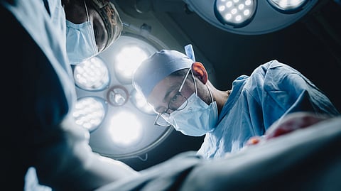 Two surgeons perform an operation under bright surgical lights.