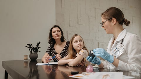 A doctor talks with a woman and a young girl while holding a medical device.