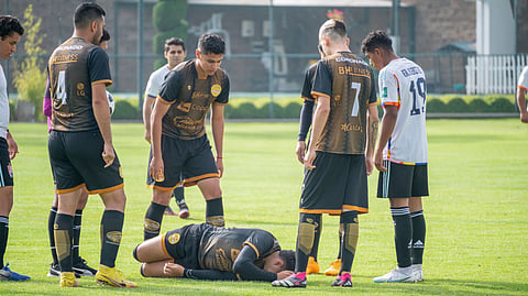 A soccer player lies injured on the field as other players gather around.