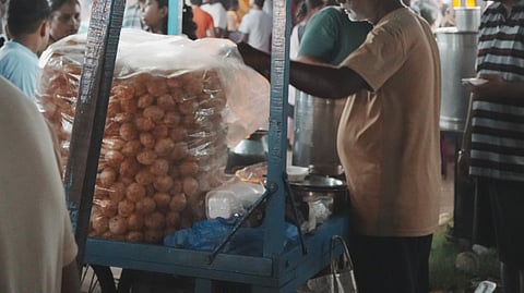 A street vendor prepares golgappas near a brightly lit temple at night.