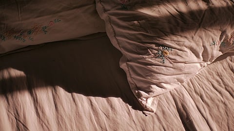 A messy bed with rumpled white sheets and floral pillows.