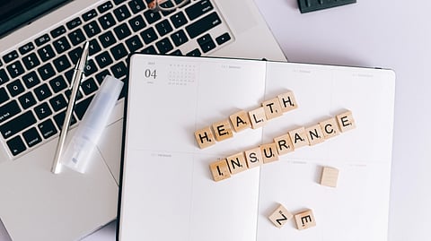 A desk with a laptop, planner, and blocks spelling “Health Insurance.”