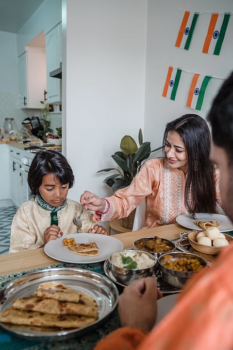 Indian mother serving a home-cooked meal of roti, curry, rice, and rasgulla to her child at the dining table