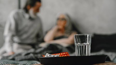 A glass of water and medicine blister packs on a black tray.