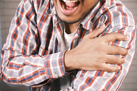 Close-up of a man in plaid shirt experiencing shoulder pain, grasping his arm.
