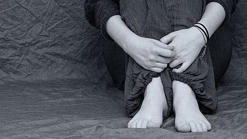 A black-and-white close-up of a person sitting with their knees hugged to their chest.