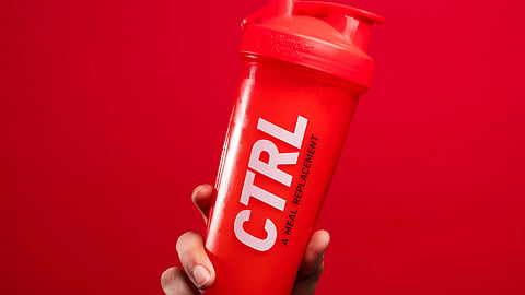 A hand holding a red CTRL brand shaker bottle against a solid red background.