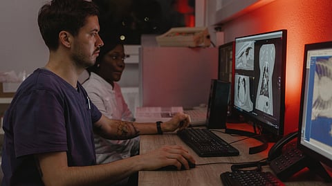 A veterinarian reviews animal CT scans on a computer while a colleague looks on.