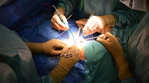 Surgeons' gloved hands performing a medical procedure.