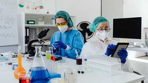 Two scientists work in a laboratory with test tubes, a microscope, and a tablet.