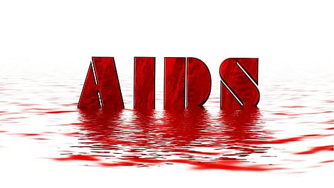 The image shows the word "AIDS" in bold, red letters half-submerged in a reflective, red-liquid surface.
