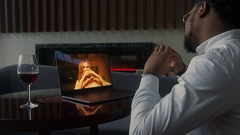 A man in a white shirt looks at a laptop during a video call.