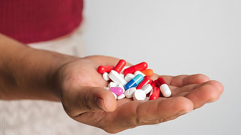 A hand holding assorted pills and capsules, including white tablets and colorful capsules.