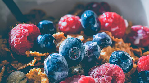 A bowl of cereal topped with fresh blueberries and raspberries.