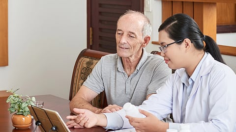 An older man sits with a doctor, discussing his healthcare at a table.