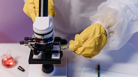 A scientist in a lab coat adjusts a slide under a microscope.