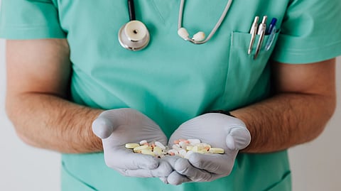 A healthcare worker in scrubs holds a handful of different pills while wearing gloves.