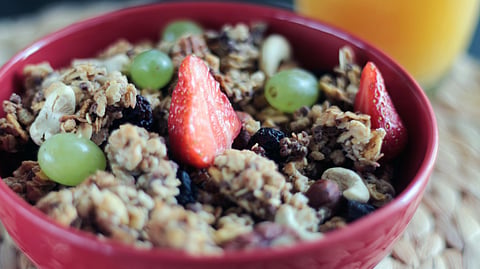A bowl of granola topped with grapes, strawberries, raisins, and cashews.