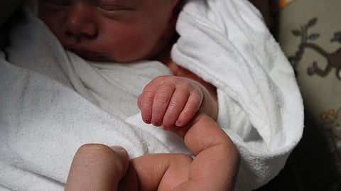 A newborn's tiny hand gently grasps an adult's finger.