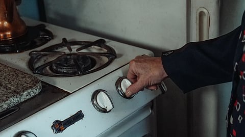 A hand turns the knob on a vintage gas stove.
