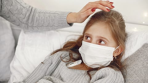 An adult comforts a young girl wearing a face mask while resting in bed.