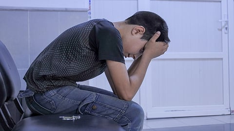 A person sits with their head in their hands, looking stressed and upset.