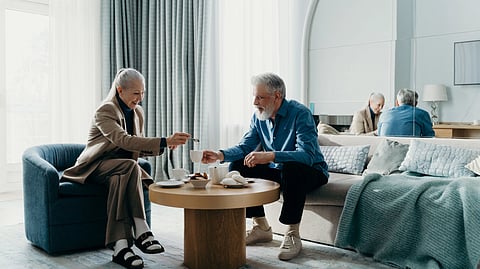 An older man and woman sitting in a modern, well-lit living room having tea.