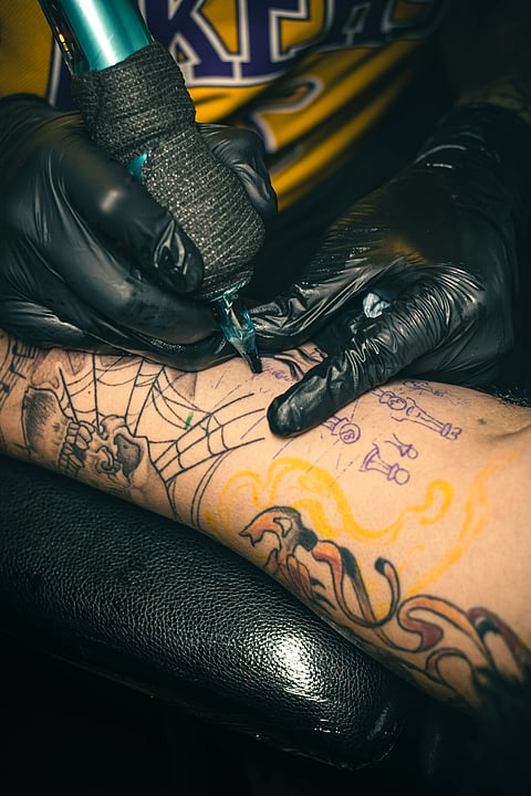 Tattoo artist using a machine to ink a design on a client's forearm